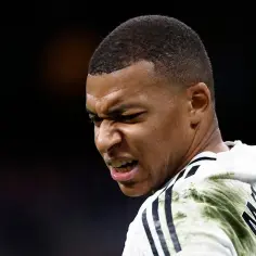 Zbliżenie na twarz Kyliana Mbappé w białej koszulce z czarnymi pasami i zielonym wzorem.